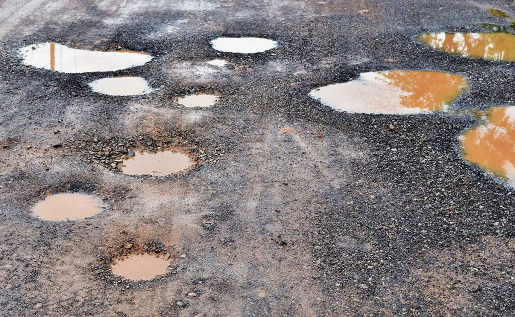 potholes in a gravel driveway needs repair filled with water