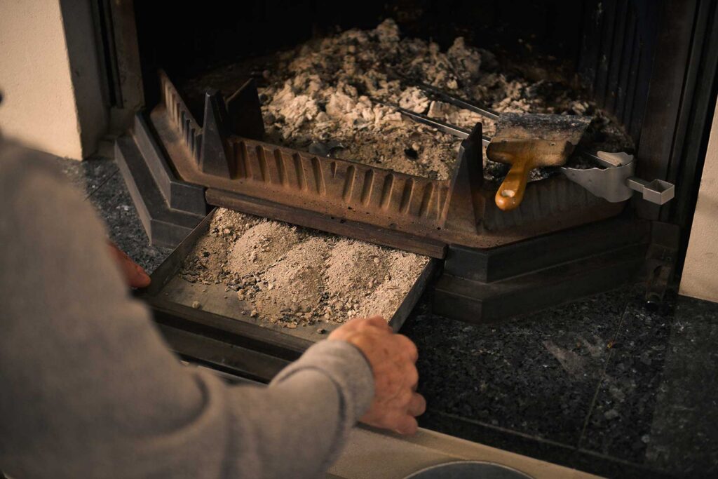 Hands emptying the ash drawer of a fireplace