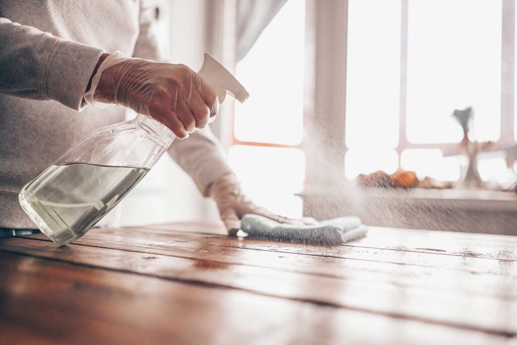 Wiping down a wooden table with spray cleaner and a towel