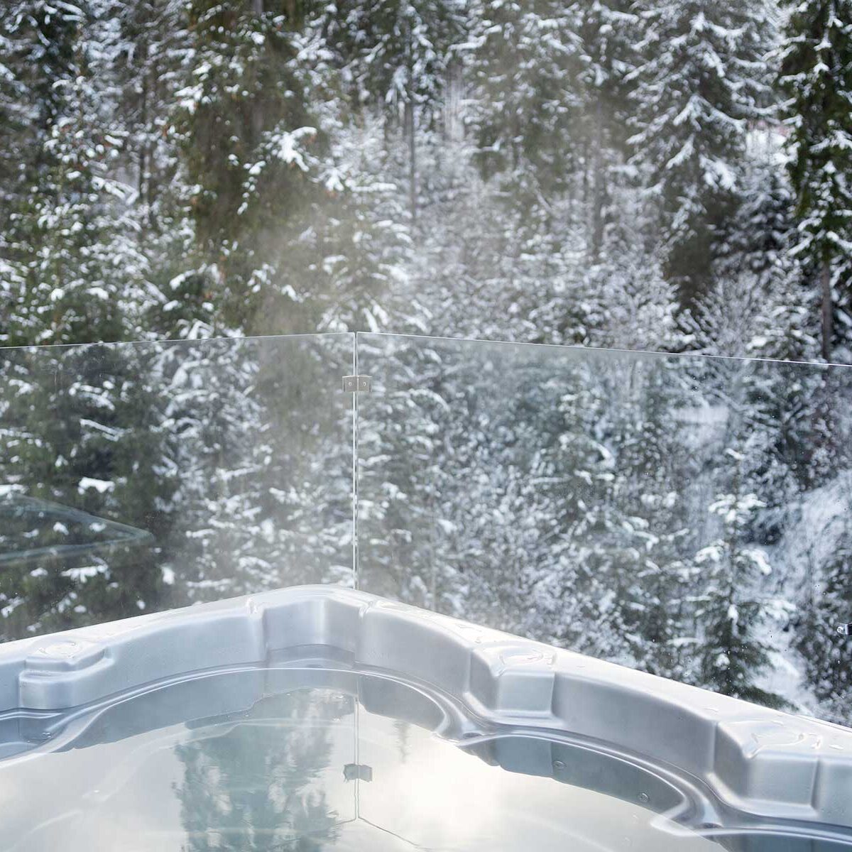 Steaming hot tub on a deck surrounded by snow-covered trees
